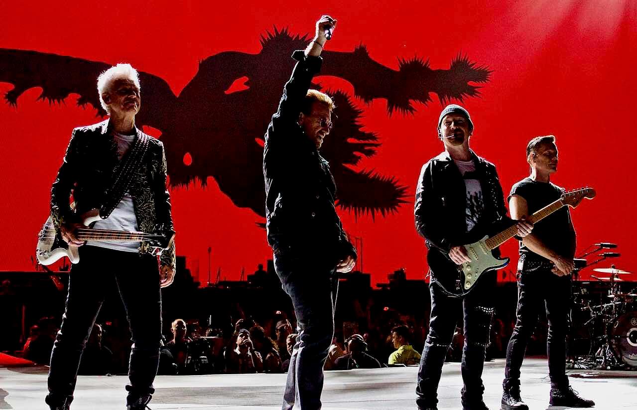 Seluruh personel U2 berada di atas panggung dengan background merah